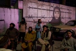 Anggota Taliban duduk di depan mural bergambar perempuan di belakang pagar kawat berduri di Kabul, Afghanistan, 21 September 2021.