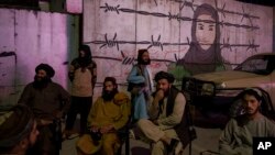 Taliban members sit in front of a mural depicting a woman behind barbed wire in Kabul, Afghanistan, Sept. 21, 2021.