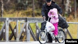 A man pushes a girl across the border from Russia to Norway on a bicycle with flat tires at the Storskog border station in northern Norway, Oct. 13, 2015. Migrants entering Norway via Russia must travel by bicycle to comply with a Russian law barring trav