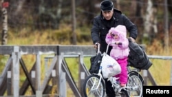 Un homme et sa fille à la station frontalière russe de Storskog dans le nord de la Norvège le 13 Octobre 2015. La loi norvégienne oblige Les migrants à voyager en vélo. Source: Reuters 