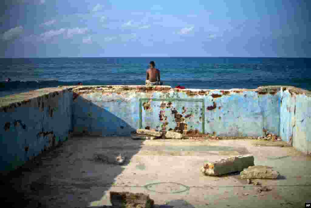 A young man looks at the sea sitting on the wall of an old abandoned pool in Cojimar, Cuba.