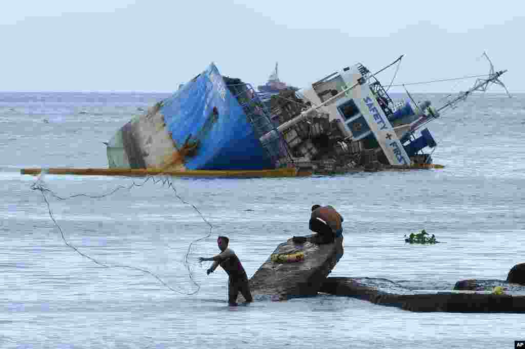 A fisherman throws his net beside the half-submerged M/V Palawan Pearl after it collided with a Cyprus-flagged BKM 104 dredger in Manila bay, Philippines.