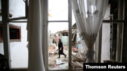 A woman walks past a house damaged by recent shelling during a military conflict over the breakaway region of Nagorno-Karabakh, in the city of Ganja, Azerbaijan, Oct. 6, 2020.