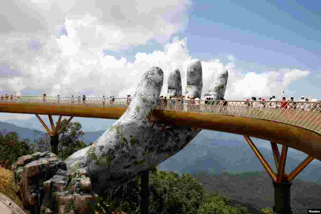 Tourists walk past a giant hand structure on the Gold Bridge on Ba Na hill near Danang City, Vietnam, Aug. 1, 2018.