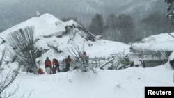 Members of Lazio's Alpine and Speleological Rescue Team stand in front of the Hotel Rigopiano in Farindola, Italy, that was hit by an avalanche, Jan. 19, 2017.