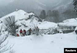 Members of Lazio's Alpine and Speleological Rescue Team stand in front of the Hotel Rigopiano in Farindola, Italy, that was hit by an avalanche, Jan. 19, 2017.