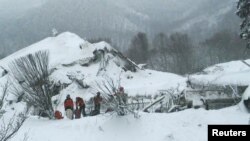 Members of Lazio's Alpine and Speleological Rescue Team stand in front of the Hotel Rigopiano in Farindola, Italy, that was hit by an avalanche, Jan. 19, 2017.