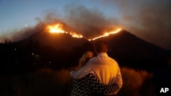 Roger Bloxberg, right, and his wife, Anne, hug as they watch a wildfire on a hill top near their home, Nov. 9, 2018, in West Hills, Calif.