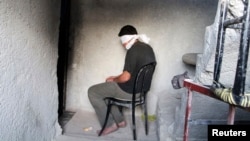 FILE - A blindfolded man suspected of passing on military information to the Syrian government waits to be interrogated after being arrested by Free Syrian Army (FSA) fighters, inside an FSA-run prison in Aleppo.