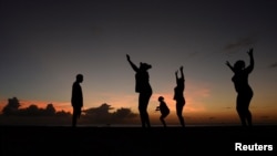 FILE - Women exercise in front of a trainer (L) as the sun sets near Kensington Oval in Bridgetown, Barbados, March 13, 2014. 