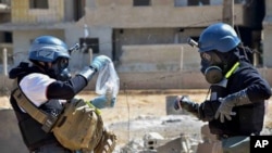In this Aug. 28, 2013 citizen journalism file image, members of a chemical weapons investigation team take samples from sand near a part of a missile that is likely to be one of the chemical rockets, according to activists, in the Damascus countryside of Ain Terma, Syria. (AP Photo/United Media office of Arbeen, File)