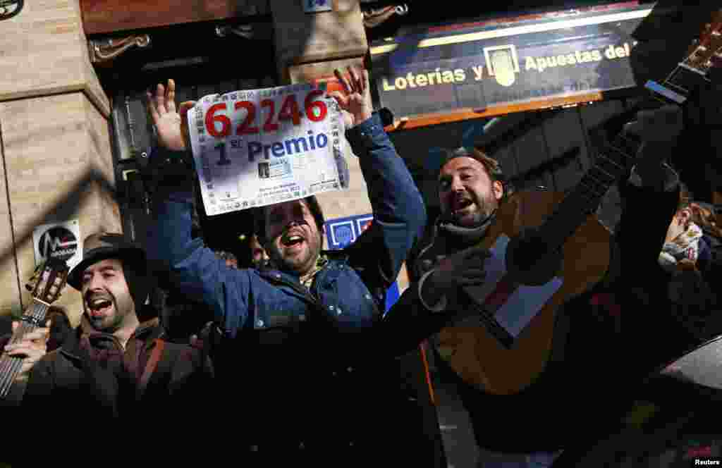 People sing as they show a poster of the winning number to the first prize of Spain&#39;s Christmas Lottery &quot;El Gordo&quot; (The Fat One) outside a lottery shop where the lottery number was sold in Sanlucar la Mayor, southern Spain. 