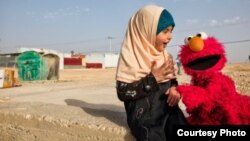 Elmo mengunjungi seorang gadis kecil di sebuah kamp pengungsi. International Rescue Committee dan Sesame Workshop – LSM yang berada di balik program televisi “Sesame Street” – memutuskan untuk membawa pendidikan langsung pada anak-anak pengungsi. (Foto: Sesame Workshop).