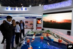 Staff members from the China National Nuclear Corporation attend foreign visitors as they look at the models of oil tanker shaped floating nuclear reactors and oil rigs showcased at the display booth of China's state-owned CNNC.