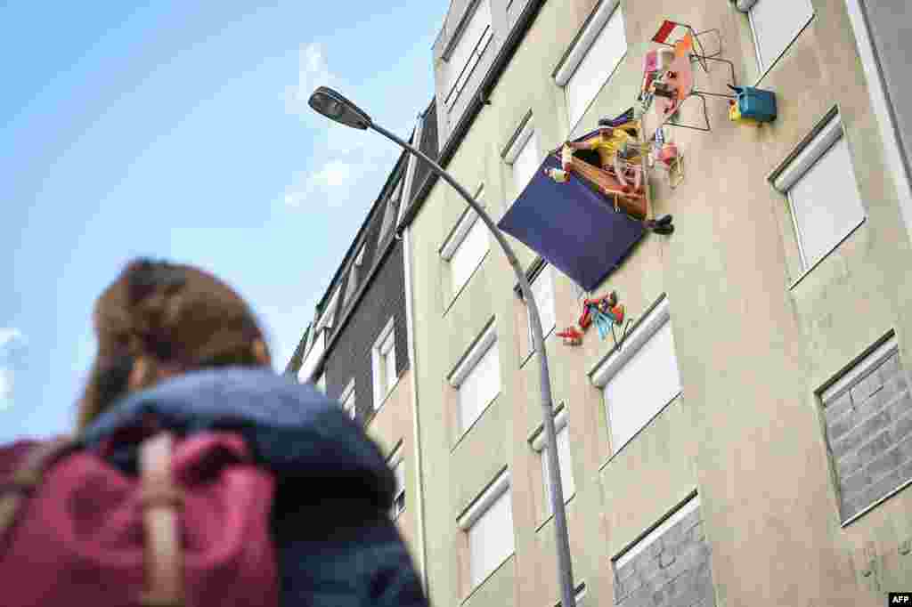 A passerby watches an actor with the French street theater company Royal de Luxe, known as 'Monsieur Bourgogne,' as he sits in his tent on the facade of a building in the Bellevue neighborhood in Saint-Herblain, near Nantes, France.