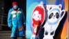 A woman wearing a face mask to protect against COVID-19 stands next to figures of the Winter Paralympic mascot Shuey Rhon Rhon left, and Winter Olympic mascot Bing Dwen Dwen on a street in Beijing, Jan. 15, 2022.