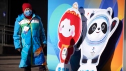 A woman wearing a face mask to protect against COVID-19 stands next to figures of the Winter Paralympic mascot Shuey Rhon Rhon left, and Winter Olympic mascot Bing Dwen Dwen on a street in Beijing, Jan. 15, 2022.