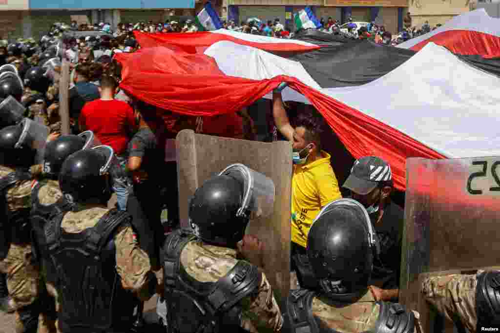 Iraqi security forces stand in front of demonstrators in anti-government protests during Iraqi Prime Minister Mustafa al-Kadhimi&#39;s visit, in Basra.