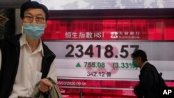 A man wearing a face mask walks past a bank's electronic board showing the Hong Kong share index at Hong Kong Stock Exchange Wednesday, March 25, 2020.