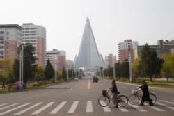 Warga mengenakan masker saat melintasi jalan di depan Hotel Ryugyong di Pyongyang, Korea Utara, 28 April 2020. (AP Photo/Cha Song Ho)