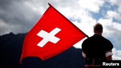 FILE - A man dressed in traditional costume holds a Swiss flag at the 28th Federal Yodeling Festival in Interlaken, Switzerland, June 19, 2011.