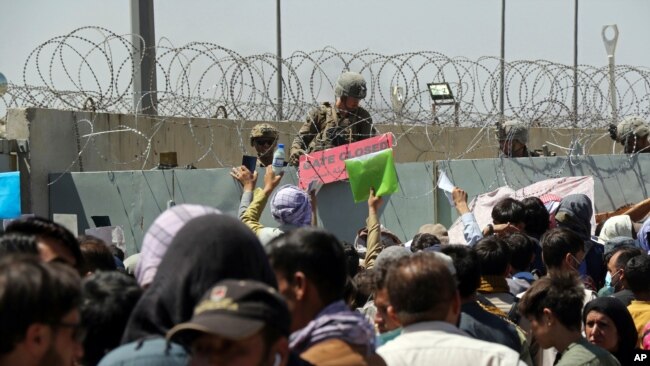 FILE - U.S. soldier holds a "Gate Closed" sign as hundreds of people gather near an evacuation checkpoint on the perimeter of Hamid Karzai International Airport, in Kabul, Afghanistan, Aug. 26, 2021.