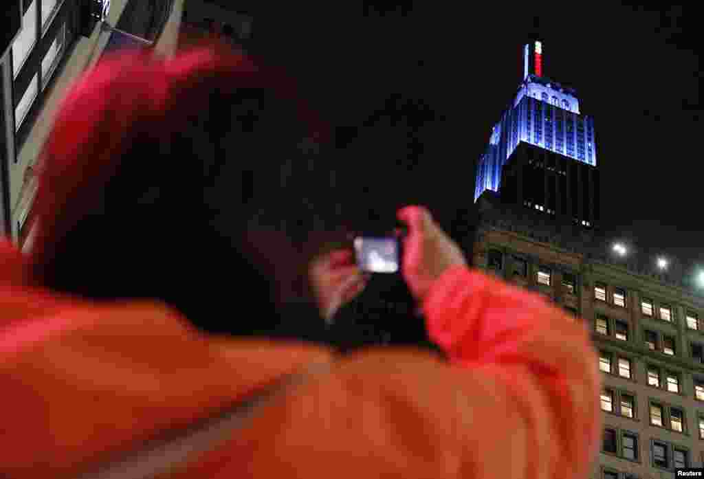 Mulher em Nova Iorque fotografa o Empire State Building, decorado com a cor azul do Partido Democr&aacute;tico, para assinalar a vit&oacute;ria de Obama