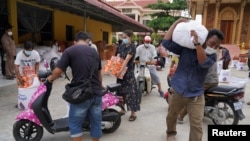 People carry sacks of rice and other food donated by the local government inside a red zone with strict lockdown measures during the latest outbreak of the coronavirus disease (COVID-19) in Phnom Penh, Cambodia, April 30, 2021. REUTERS/Cindy Liu