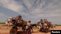 FILE - A Sudanese woman, who fled the conflict in Murnei in Sudan's Darfur region, walks beside carts carrying her family belongings upon crossing the border between Sudan and Chad in Adre, Chad August 2, 2023.