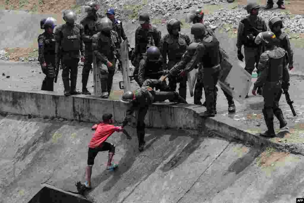 Members of the Boliviarian Guard prevent a child from collecting water from a sewage canal at the river Guaire in Caracas, as a massive power outage continues affecting some areas of the country.