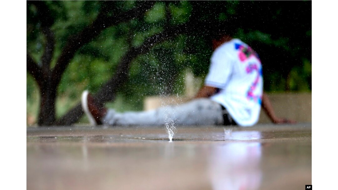 FILE - A man tries to keep cool on a children's splash pad, June 25, 2024 in Phoenix.