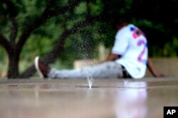 FILE - A man tries to keep cool on a children's splash pad, June 25, 2024 in Phoenix.