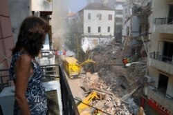 A woman stands on her balcony as she looks at rescuers searching at the site of a collapsed building in Beirut, Lebanon, Sept. 4, 2020.