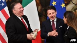U.S. Secretary of State Mike Pompeo, left, holds a package of Parmesan cheese as Italy's Prime Minister Giuseppe Conte reacts, after the package was handed to Pompeo by Italian journalist Alice Martinelli, right, in Rome, Oct. 1, 2019. 