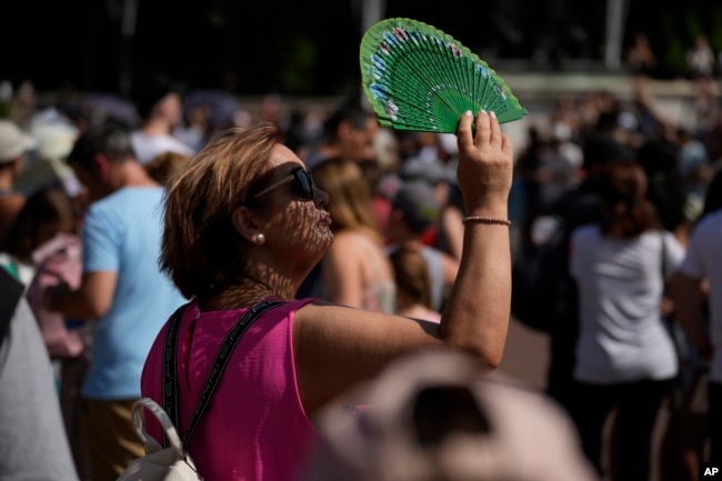 A tourist uses a fan to shade her face from the sun whilst waiting to watch the Changing of the Guard ceremony outside Buckingham Palace, during hot weather in London, July 18, 2022. (AP Photo/Matt Dunham, File)