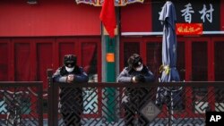 In this Feb. 23, 2020, photo, security guards wearing protective face masks browse their smartphones near shuttered business shops in Beijing. 