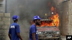 Pakistani volunteers look at a vehicle that was set on fire by an angry mob in Karachi, Pakistan, August 1, 2011