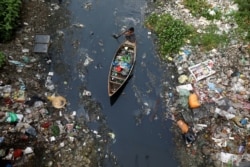 FILE - A man on a boat collects plastic materials from dirty water in Dhaka, Bangladesh, April 17, 2019.