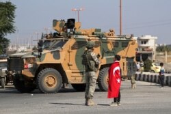 A boy wearing a Turkish flag stands next to a Turkish soldier in the town of Tal Abyad, Syria, Oct. 23, 2019.