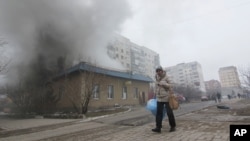 Žena prolazi pored zgrade u plamenu u Marijupolju