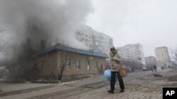 A woman resident passes by a burning house in Mariupol, Ukraine, Jan. 24, 2015.
