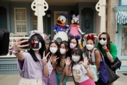 Visitors wearing face masks take a selfie with the iconic cartoon characters Donald Duck and Daisy Duck at the Hong Kong Disneyland, Sept. 25, 2020.