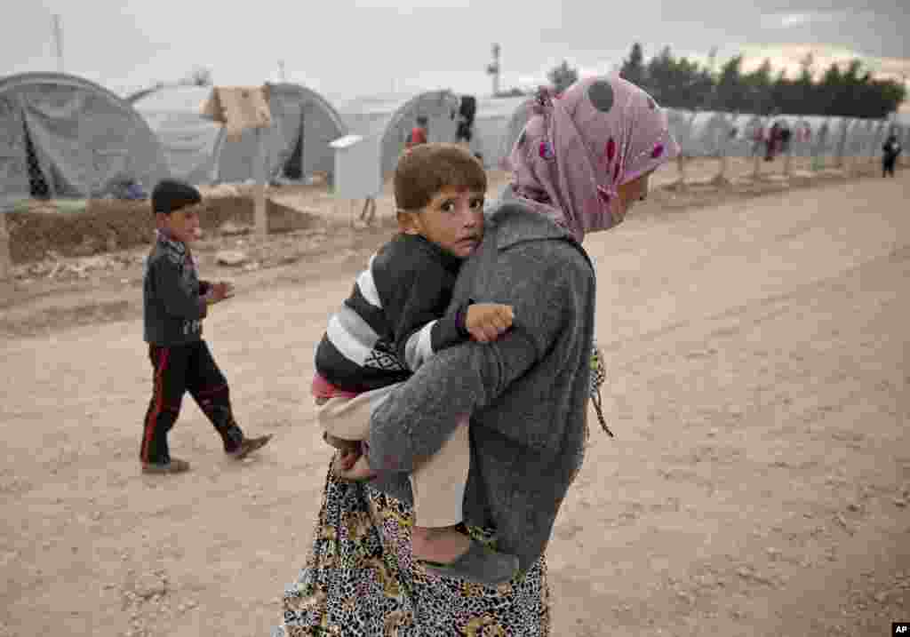 A Syrian Kurdish refugee from Kobani carries a young child, at a refugee camp in Suruc, Turkey, Oct. 23, 2014. 