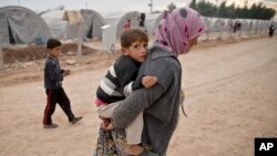 A Syrian Kurdish refugee woman from Kobani, carries a baby at a refugee camp in Suruc, near the Turkey-Syria border, Oct. 23, 2014. 