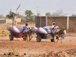 FILE - Displaced women, who fled from attacks by armed militants in the town of Roffenega, ride donkey carts loaded with food aid in the city of Pissila, Burkina Faso, Jan. 23, 2020.