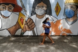 FILE - A woman wearing protective mask to prevent the spread of the coronavirus walk past a mural showing frontliners in Manila, Philippines on Oct. 21, 2020.