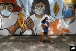 FILE - A woman wearing protective mask to prevent the spread of the coronavirus walk past a mural showing frontliners in Manila, Philippines on Oct. 21, 2020.
