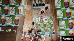 Seorang pria mengendarai sepeda melewati poster-poster kampanya di Bamako (9/8).