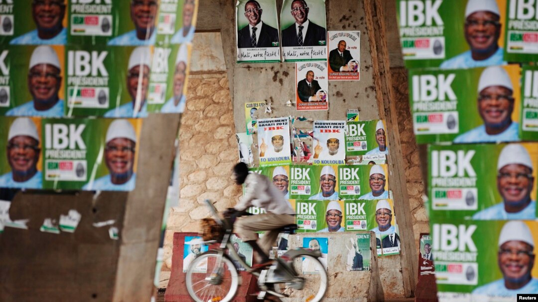 Seorang pria mengendarai sepeda melewati poster-poster kampanya di Bamako (9/8).