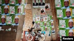 Seorang pengendara sepeda melintasi poster-poster dua kandidat presiden Mali di Bamako (9/8).